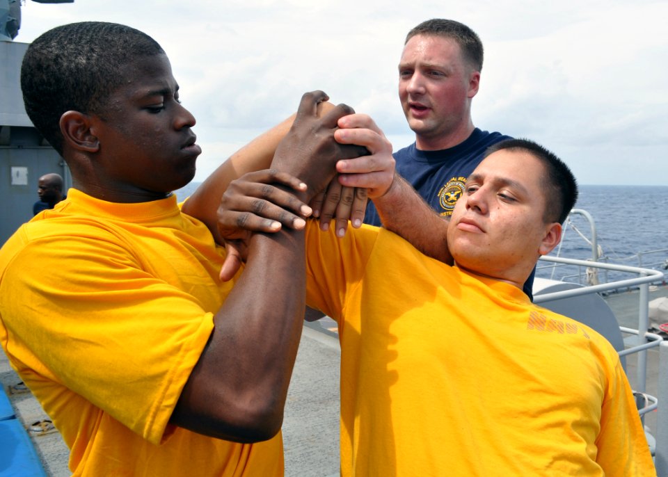 US Navy 101019-N-3620B-085 Master-at-Arms 2nd Class Alex Dorais, center, assists Quartermaster 2nd Class James Baker, left
