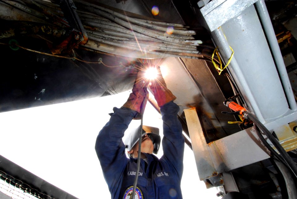US Navy 101025-N-5031T-105 Hull Maintenance Technician 2nd Class Matthew Kabisch, from Los Angeles, Calif. welds above the portside catwalk aboard