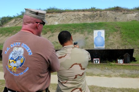 US Navy 101028-N-4936C-474 Hospital Corpsman Seaman David Blair fires a 9 mm pistol as Senior Chief Master-at-Arms John Bates looks on