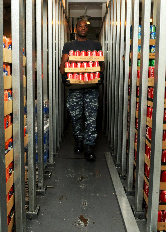 US Navy 101101-N-1004S-097 Ship's Serviceman Seaman Joshua Marshall, from Long Beach, Calif., carries cases of soda to the back of a storeroom aboa