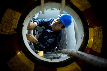 US Navy 101117-N-9643K-739 Machinist's Mate Fireman Juan Morales traces an electrical line while performing maintenance beneath the hangar bay of t