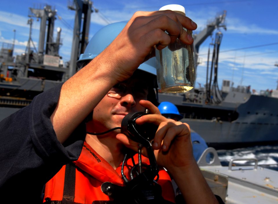 US Navy 101117-N-9706M-326 Machinist's Mate 3rd Class Robert Loughbom inspects a sample of JP-5 jet fuel aboard the amphibious transport dock ship