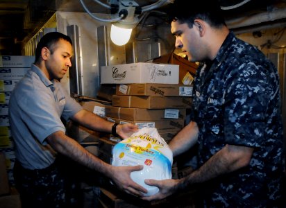 US Navy 101123-N-7095C-165 Culinary Specialist Seaman Amit Shivnani, left, hands a 15-pound turkey to Culinary Specialist 2nd Class Nisse Fonseca d