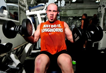 US Navy 101122-N-7948R-093 Engineman 3rd Class Joseph Rocca performs dumbbell curls in the gym aboard the amphibious dock landing ship USS Pearl Ha