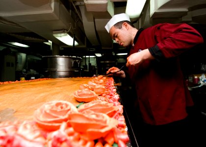US Navy 101125-N-9626Y-045 Culinary Specialist 3rd Class Adam Herron, from Houston, decorates a cake during preparations for the Thanksgiving meal