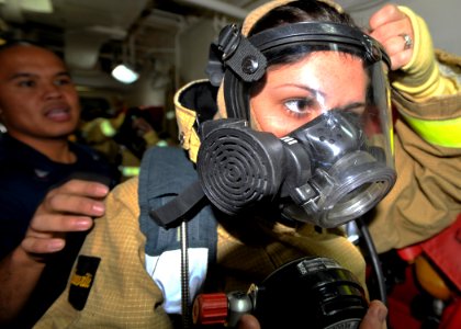 US Navy 101122-N-6499D-081 Damage Controlman 2nd Class Dean Bonoan helps Operations Specialist Seaman Kai Varela don a firefighting suit during dam