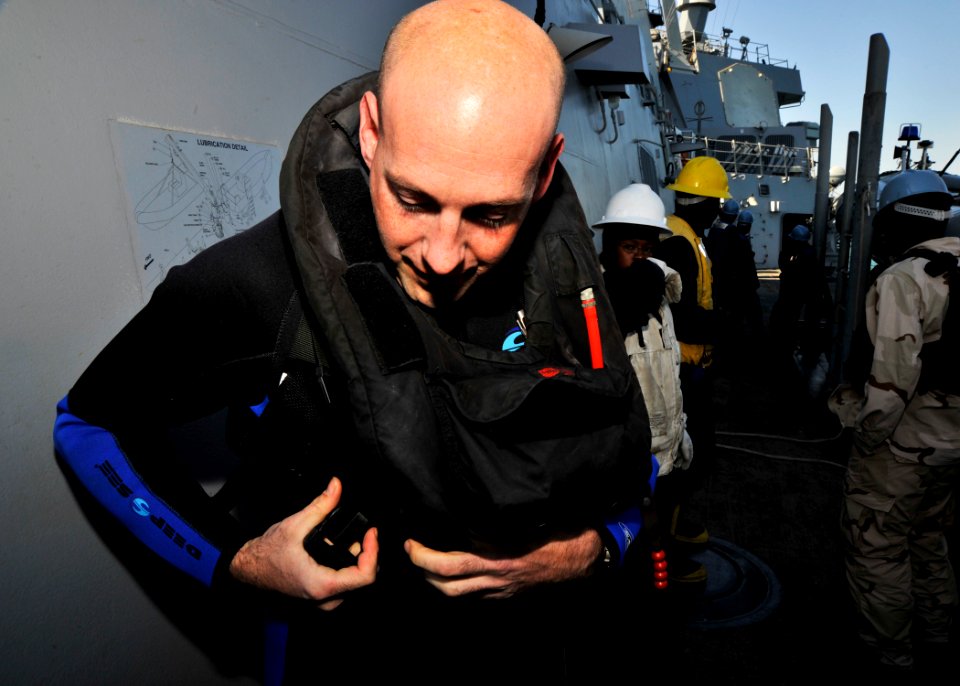 US Navy 101128-N-6499D-017 Interior Communications Electrician 1st Class Jonathon Grinols dons a life preserver before a security patrol aboard USS