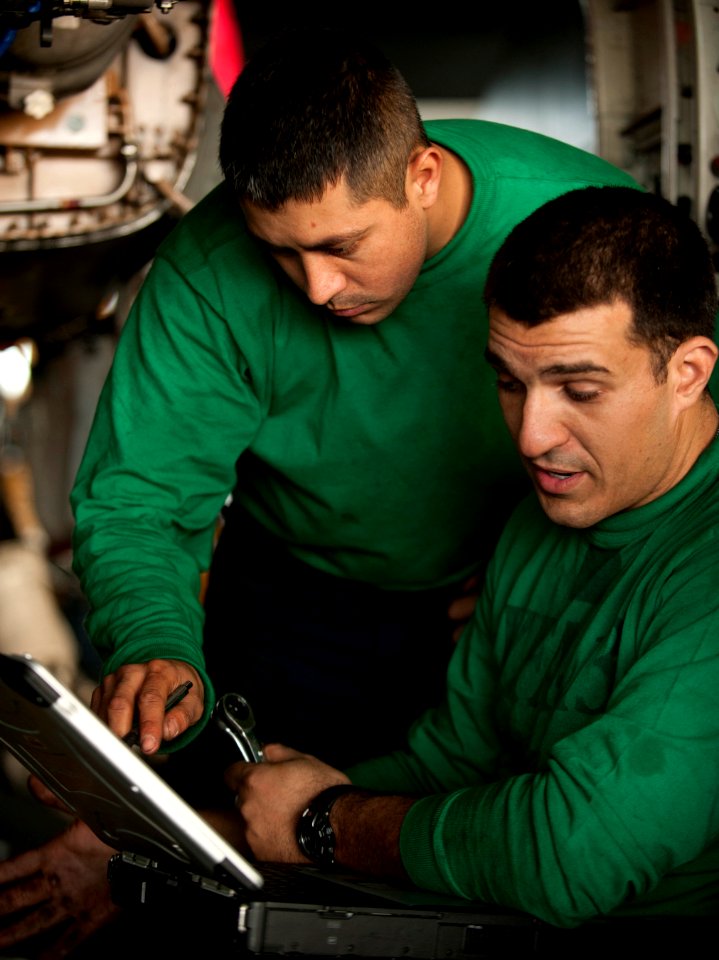 US Navy 101206-N-7981E-327 Sailors replace a fuel line on the F104-GE-400 jet engine of an F-A-18C Hornet in the hangar bay of the aircraft carrier