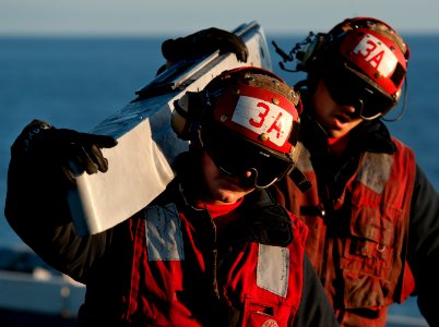 US Navy 101204-N-7981E-458 Aviation ordnancemen assigned to Strike Fighter Squadron (VFA) 113 carry a weapons pylon across the flight deck of the a