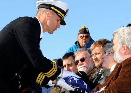 US Navy 101207-N-5812W-005 Cmdr. Craig Bowden, commanding officer of the guided-missile frigate USS Underwood (FFG 36), presents the American flag