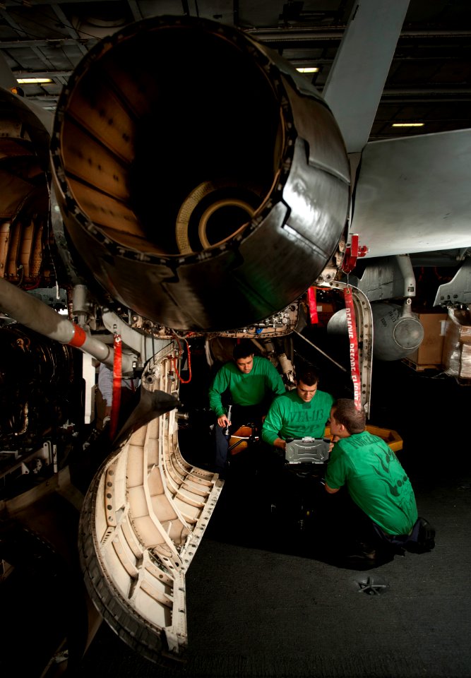 US Navy 101206-N-7981E-277 Sailors replace a fuel line on the F104-GE-400 jet engine of an F-A-18C Hornet in the hangar bay of the aircraft carrier