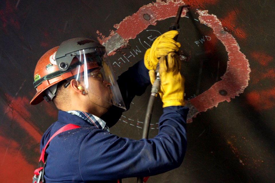 US Navy 101207-N-9643K-355 A NASSCO shipyard worker chips paint off the hull of the amphibious assault ship USS Bonhomme Richard (LHD 6)
