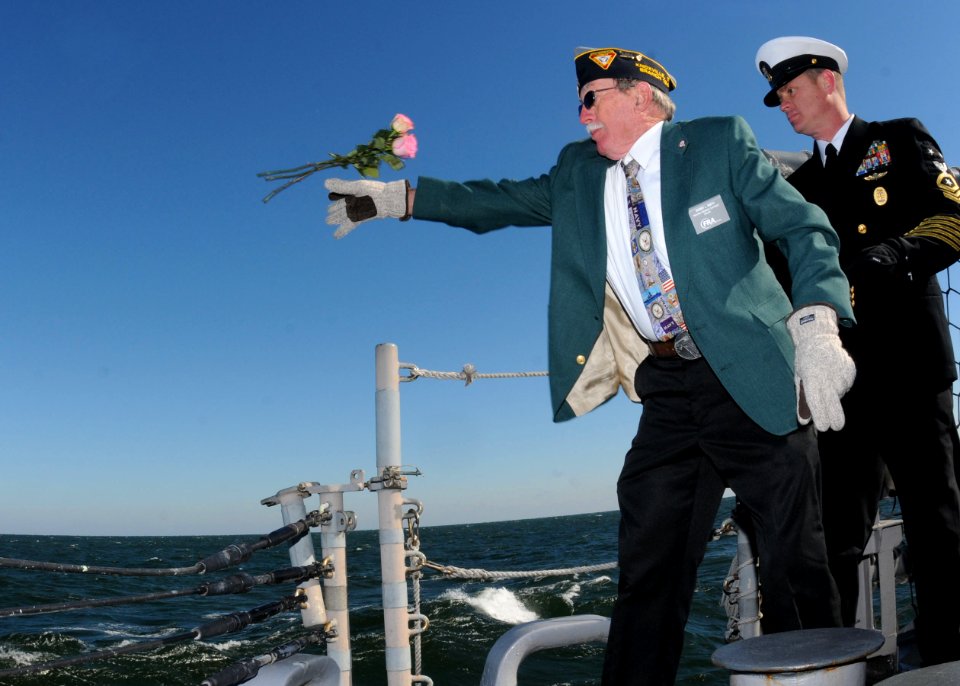 US Navy 101207-N-5812W-001 Navy veteran Bobby Smith, left, tosses roses into the ocean as Command Master Chief Matt Miesle steadies him during a Pe