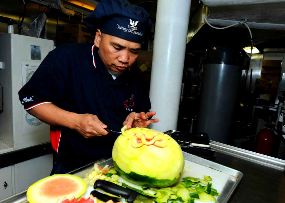 US Navy 101208-N-6632S-018 Culinary Specialist 2nd Class Rudy L. Tabayoyong, from the S-2 Division of the supply department, carves a watermelon fo