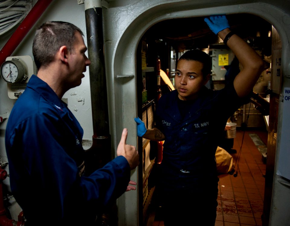 US Navy 101213-N-7981E-224 Hull Technician Fireman Jesseca Crosby discusses waste processing room hours and trash receiving policies with a Sailor