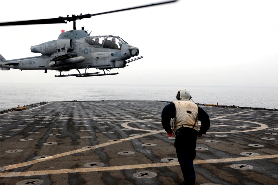 US Navy 101215-N-3659B-013 Boatswain's Mate 1st Class Adam Cohen braces himself as a AH-1 Cobra helicopter approaches USS Comstock (LSD 45)