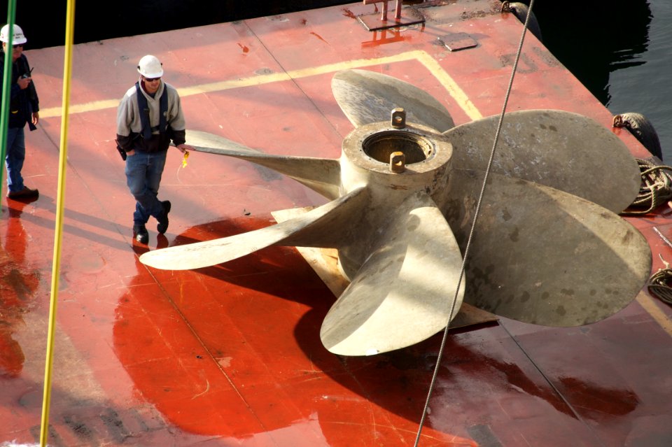 US Navy 101223-N-9643K-525 National Steel and Shipbuilding Company shipyard workers use a barge crane to move the propellers and rudder of the amph