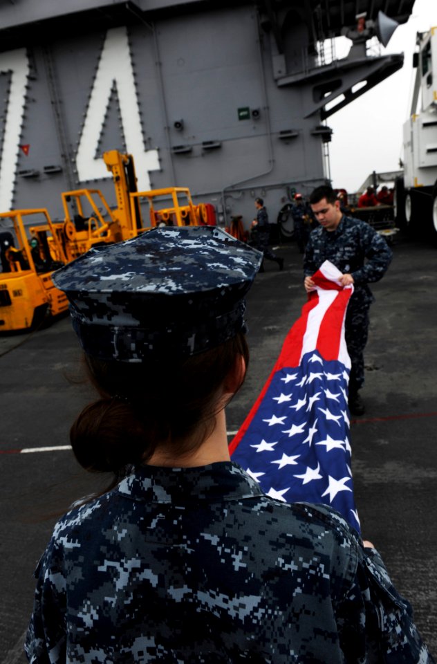US Navy 110119-N-2475A-124 Airman Katy Burgmeier and Yeoman Seaman Richard Harris fold the national ensign on the flight deck of the Nimitz-class