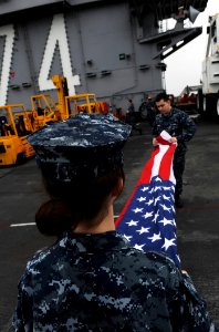 US Navy 110119-N-2475A-124 Airman Katy Burgmeier and Yeoman Seaman Richard Harris fold the national ensign on the flight deck of the Nimitz-class
