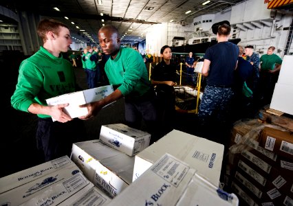 US Navy 101229-N-2055M-059 Aviation Structural Mechanic (Equipment) Airman Joshua Nunn hands a box of meat to another Sailor in the hangar bay of t