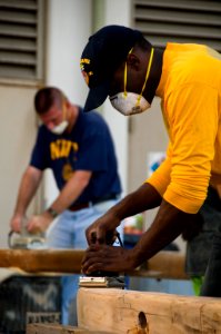 US Navy 110122-N-6674H-006 Engineman Fireman Ross McCray, front, sands down a support beam for a Polynesian canoe while Capt. Dave Welch works on t