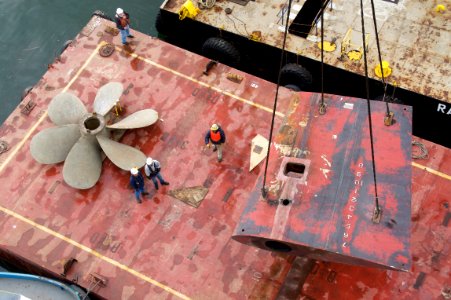 US Navy 101223-N-9643K-596 National Steel and Shipbuilding Company shipyard workers use a barge crane to move the propellers and rudder of the amph