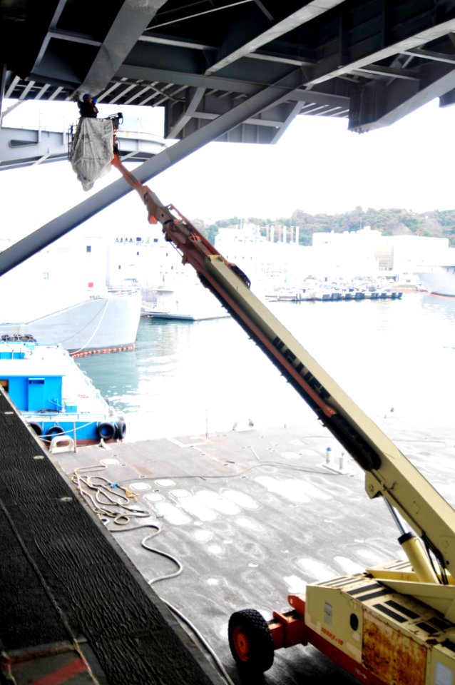US Navy 101230-N-7103C-011 Sailors use a 50-foot lifting crane to perform corrosion control maintenance underneath an aircraft elevator aboard the