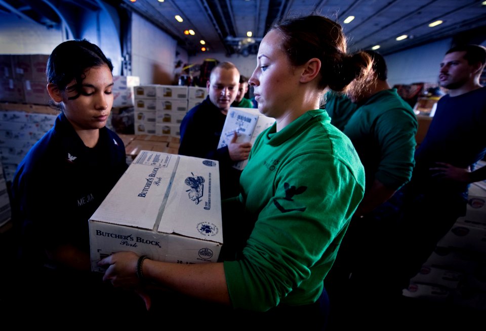 US Navy 101229-N-2055M-181 Aircrew Survival Equipmentman 3rd Class Jennifer Looney hands a box of meat to another Sailor in the hangar bay of the a
