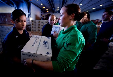 US Navy 101229-N-2055M-181 Aircrew Survival Equipmentman 3rd Class Jennifer Looney hands a box of meat to another Sailor in the hangar bay of the a