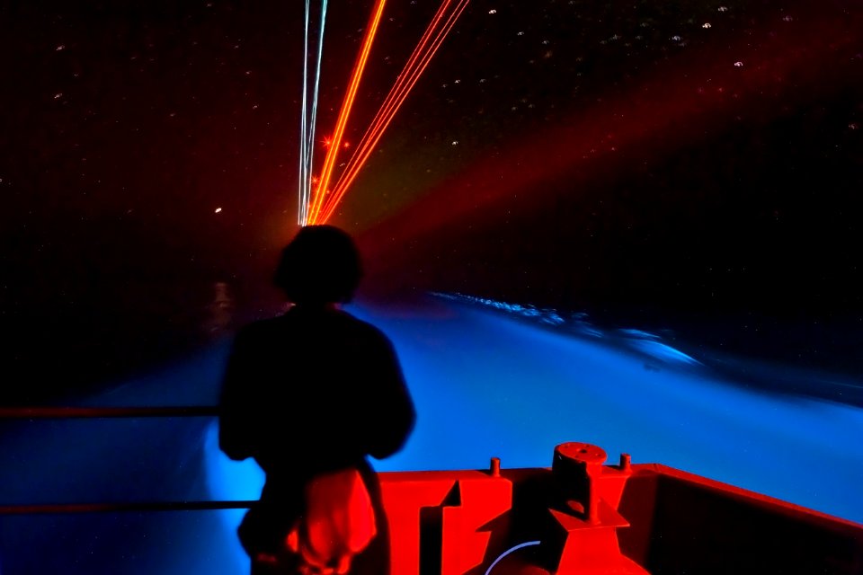 US Navy 110202-N-7981E-805 A Sailor stands watch on the fantail of the aircraft carrier USS Carl Vinson (CVN 70) as bioluminescent organisms and a