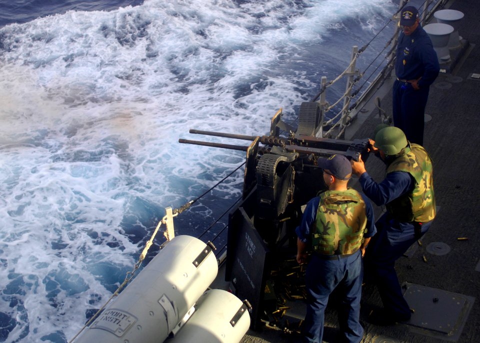 US Navy 110220-N-5838W-002 Gunner's Mate 2nd Class Edward Shoman, left, supervises Electronics Technician 2nd Class Yusuf Smith as he fires a .50-c