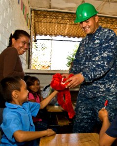 US Navy 110222-N-UX336-017 Hospital Corpsman 2nd Class Robert Medina hands a stuffed animal donated by Loving Hugs, Inc., to a student at Centro Es