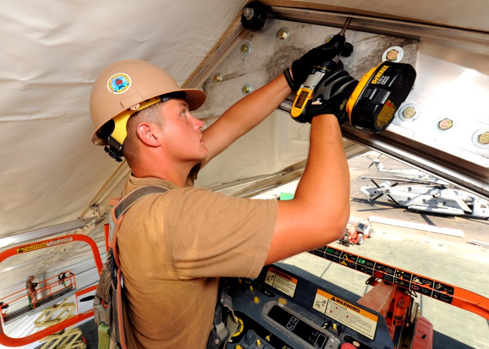 US Navy 110225-N-SN160-084 Equipment Operator Constructionman Dylan Uhls tightens bolts on a 110-foot by 130-foot tensioned-fabric aircraft hangar
