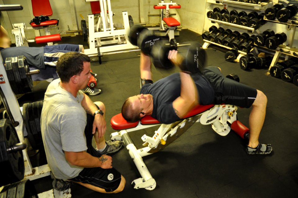 US Navy 110312-N-7293M-243 Gunner's Mate 2nd Class Joshua Leach spots Seaman Myles Stratton while lifting weights in the workout room aboard the am