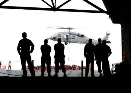 US Navy 110315-N-5538K-127 Sailors assigned to the amphibious assault ship USS Essex (LHD 2) watch as an MH-60S Sea Hawk helicopter transports huma