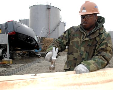 US Navy 110315-N-ZI955-063 Builder 2nd Class Charles Hannah nails two-by-four planks to reinforce the fence line at Fleet and Industrial Supply Cen