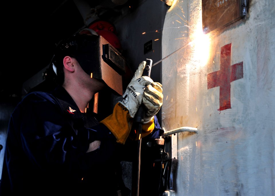 US Navy 110317-N-0074G-017 Hull Maintenance Technician 3rd Class Stephen Laroche welds a metal plate over a hole in a hatch to a medical battle dre