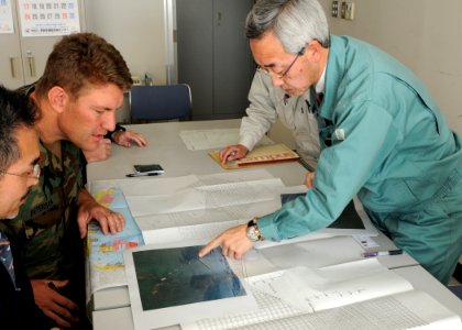 US Navy 110318-N-MU720-021 Lt. Cmdr. Derek Peterson, left, from Cocoa, Fla., a U.S. 7th Fleet salvage officer, views photos of damage caused by a t