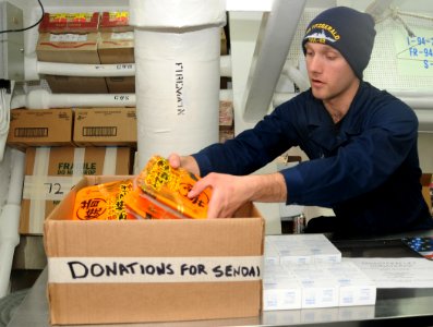 US Navy 110324-N-8288P-480 Ship's Serviceman Seaman Steven Day places food into a box set aside for donations to Sendai, Japan