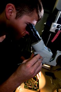 US Navy 110326-N-6320L-008 Interior Communications Electrician 3rd Class James Poole examines a circuit board in the micro miniature electronics re