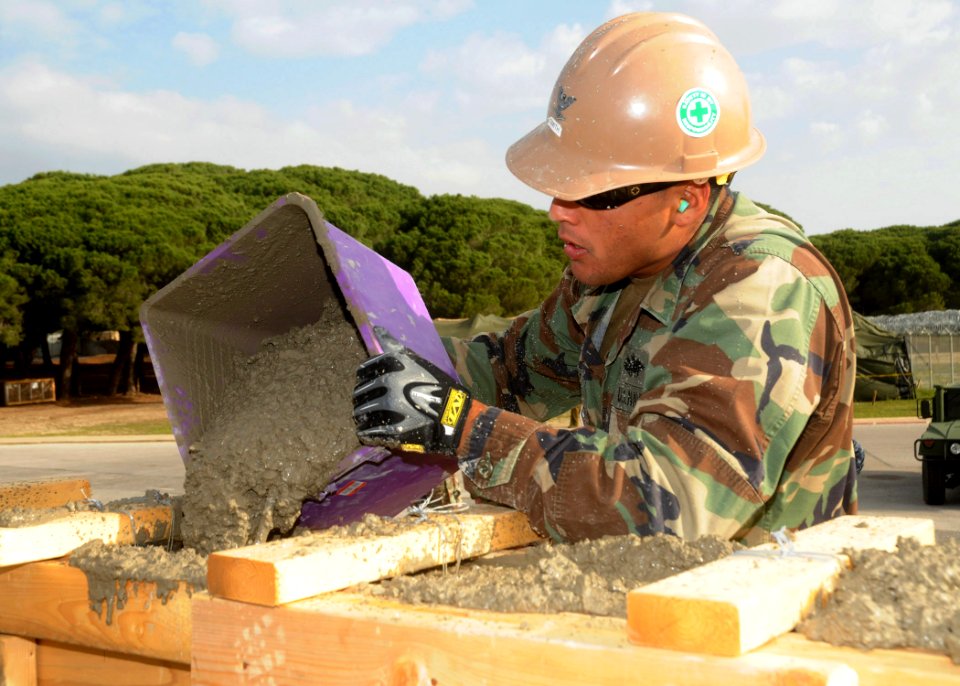US Navy 110324-N-AW868-008 Construction Electrician Constructionman Daniel Arteche pours fresh concrete into wooden forms at a bus stop project at
