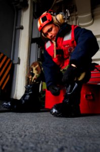 US Navy 110325-N-5538K-017 Aviation Ordnanceman 1st Class Dariel R. Hernandez dons mission oriented protective posture overboots before working on