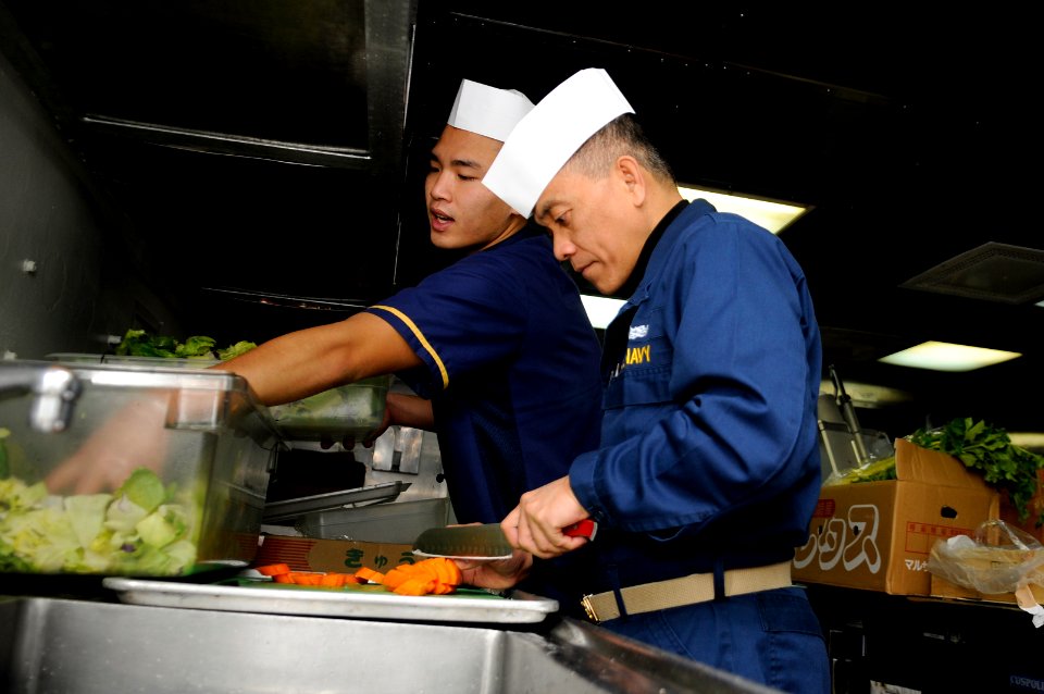 US Navy 110328-N-6692A-032 enior Chief Culinary Specialist Leo Miranda, right, assists in galley operation aboard USS Germantown (LSD 42)