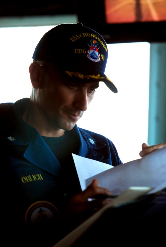 US Navy 110330-N-WP746-137 Cmdr. Justin Orlick reviews paperwork on the bridge aboard USS Chung-Hoon (DDG 93)