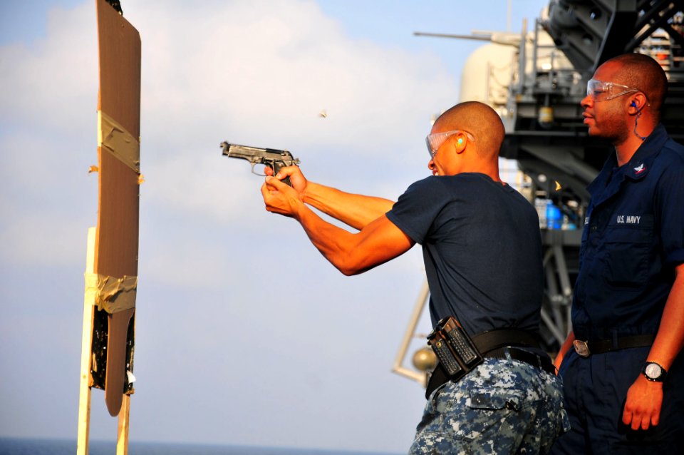 US Navy 110406-N-ZS026-059 Aviation Ordnanceman 3rd Class Rayjuan Horton fires a 9mm pistol from behind cover during a small arms practical weapons