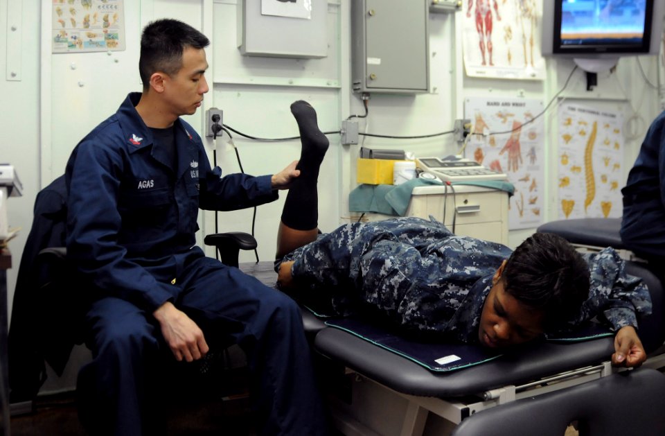US Navy 110407-N-8288P-009 Hospital Corpsman 2nd Class Emil Agas pulls and pushes the knee joint of a Sailor during a physical therapy session in t