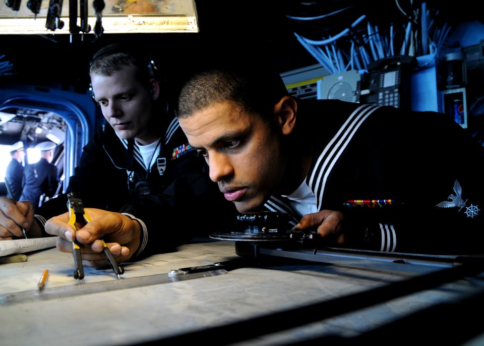US Navy 110414-N-RU841-040 Quartermaster 3rd Class Elvis Gomez, right, checks a navigation chart while Quartermaster 2nd Class Kevin Bell makes a l