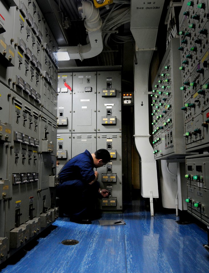 US Navy 110418-N-7488A-070 Electrician's Mate Fireman Juan Jose Murillo checks indicating lights in load center 3 while standing load center rover