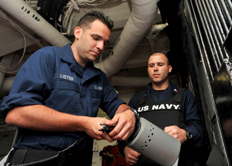 US Navy 110501-N-0569K-012 Logistics Specialist Seaman Terry J. Lister, left, uploads a 9 mm pistol in preparation for his shift while Master-at-A