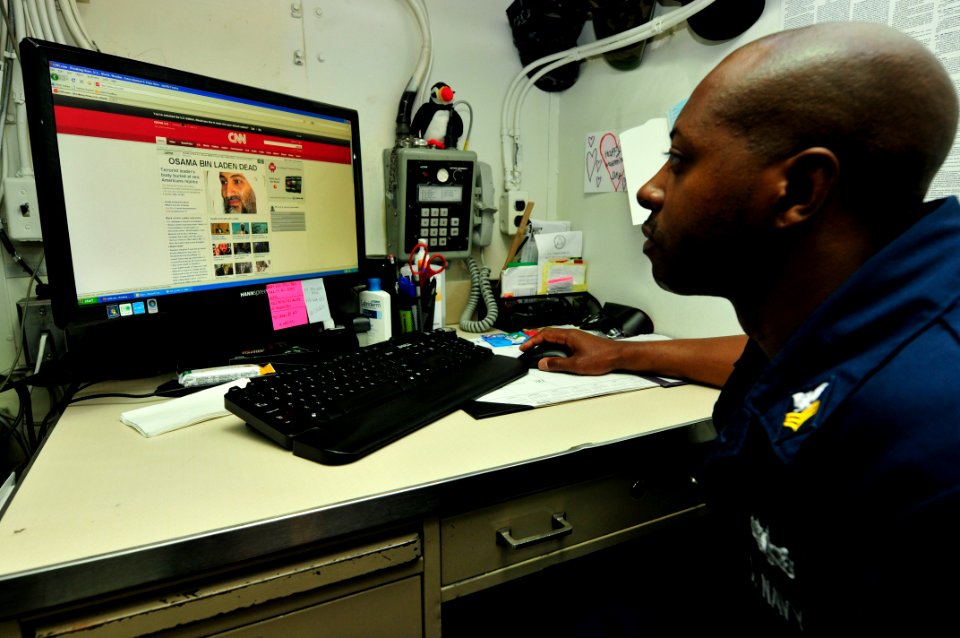 US Navy 110502-N-XO436-001 Master-at-Arms 1st Class Kelvin Lee reads about Osama Bin Laden's death while reading the morning news aboard the guided